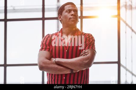Portrait eines jungen Mannes, der in einem Büro wegschaut und im Büro mit gekreuzten Armen steht. Stockfoto