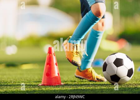 Beine eines Fußballspielers in blauen Socken und Stollen, die mit dem Ball laufen und dribbeln. Kinder beim Fußballtraining. Fußballspieler läuft die Ba Stockfoto