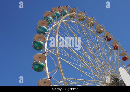 Ein Riesenrad steht majestätisch vor dem blauen Himmel, beleuchtet von leuchtenden grünen und roten Kugeln Stockfoto