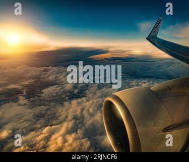 Ein Blick aus der Luft auf Wolken bei goldenem Sonnenuntergang aus dem Flugzeugfenster Stockfoto