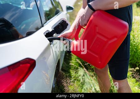 Der Fahrer füllt den leeren Tank des Fahrzeugs aus einem roten Kanister am Straßenrand Stockfoto