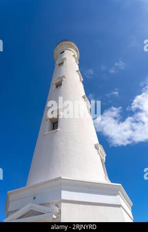 Ein majestätischer weißer Leuchtturm steht hoch vor dem Hintergrund eines wunderschönen blauen Himmels und flauschiger weißer Wolken und schafft eine atemberaubende und ruhige Szene Stockfoto