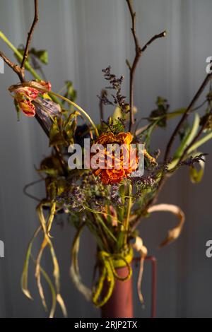 Ein getrockneter Blumenstrauß in einer Tonvase, der an einer weißen Wand steht Stockfoto