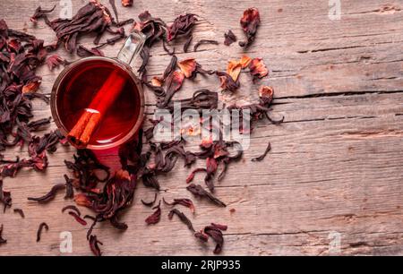Eine bis zum Rand gefüllte Glasschale mit einem leuchtend roten Hibiskus-Tee, mit ein paar trockenen Teeblättern, die um die Tasse verstreut sind Stockfoto