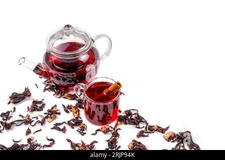 Eine bis zum Rand gefüllte Glasschale mit einem leuchtend roten Hibiskus-Tee, mit ein paar trockenen Teeblättern, die um die Tasse verstreut sind Stockfoto