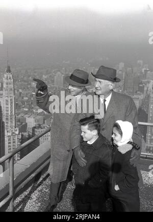 1940er Jahre, historisch, eine Familie hoch oben auf einem New Yorker Wolkenkratzer mit Blick auf die Skyline der Stadt, NYC, USA. Alles in Mänteln und die beiden Männer, die Hüte tragen, ein häufiger Anblick in dieser Ära. Stockfoto