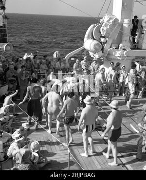 Um die späten 1960er Jahre, historische Passagiere auf dem Deck eines Kreuzfahrtschiffes, die Spaß haben, an der Zeremonie teilzunehmen, wenn ihr Kreuzfahrtschiff den Äquator überquert, während andere Passagiere beobachten. Die Zeremonie „Überquerung der Linie“ oder „Seetaufe“ ist eine der bekanntesten Traditionen, wenn ein Schiff den Äquator überquert. Stockfoto