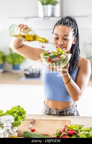 Eine junge afroamerikanische Frau bereitet einen gesunden Blattsalat zu, den sie mit Olivenöl vergießt. Stockfoto