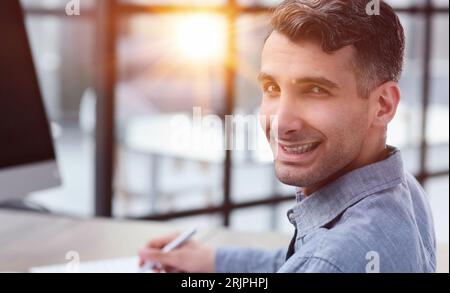 Porträt des jungen Mannes sitzt an seinem Schreibtisch im Büro Stockfoto