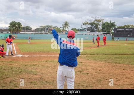Ein junger Mann, der ein blau-rotes Baseballtrikot und eine Uniform trägt, steht auf einem Feld und zeigt auf einem Spielfeld Stockfoto