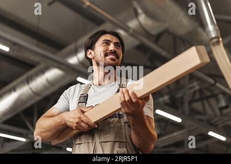 Junger Zimmermann sucht und wählt Holzbohle in einer Werkstatt in einer Holzfabrik Stockfoto