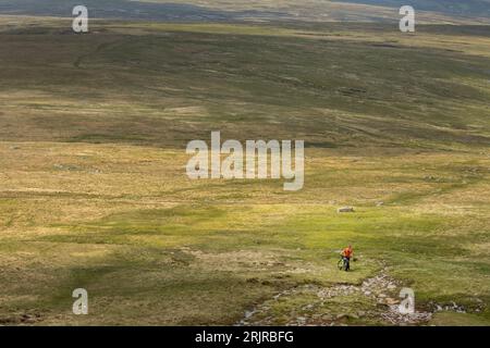 Radfahrer mit dem Mountainbike auf der rauen und einsamen Strecke hinauf zum Gipfel des Cross Fell, dem höchsten Punkt der Pennines, Eden Valley, Cumbria Stockfoto