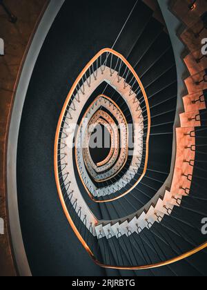 Ein erhöhter Blick auf eine moderne Wendeltreppe mit schwarzer Treppe und einem Metallgeländer. Stockfoto
