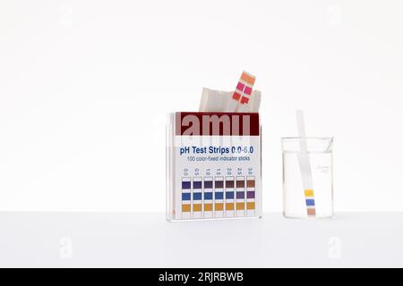 Weißer Hintergrund mit Teststreifen zur pH-Wert-Prüfung und einem Glas Säure Stockfoto