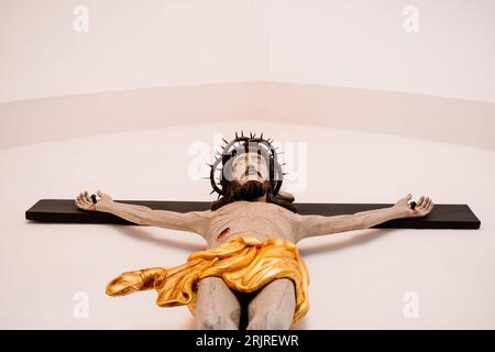 Sculpture of a crucified Christ, on a white wall, seen from below. Stock Photo