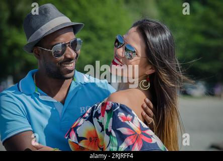 Ein fröhlicher junger Mann und eine fröhliche Frau, die stilvolle Sonnenbrillen tragen, nebeneinander stehen und zusammen lächeln. Stockfoto