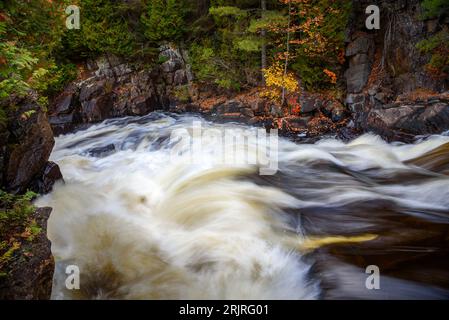 Fast flowing water at the top of a waterfall along a river running through a forest in autumn Stock Photo
