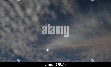 Ein Nachthimmel voller flauschiger Wolken, die von Sternenlicht beleuchtet werden. Stockfoto