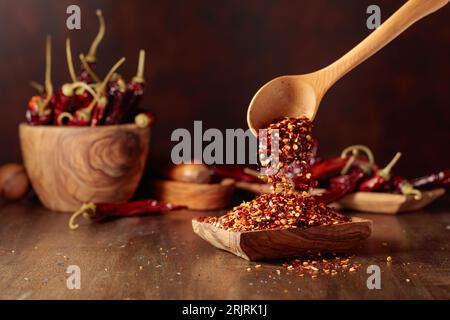 Chiliflocken werden in eine Holzschale gegossen. Chiliflocken und getrocknete Chilischoten auf einem alten Holztisch. Stockfoto