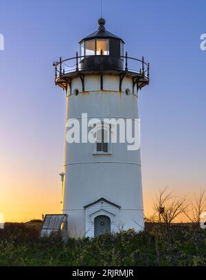 Ein weißer Leuchtturm steht hoch im goldenen Sonnenlicht einer untergehenden Sonne Stockfoto