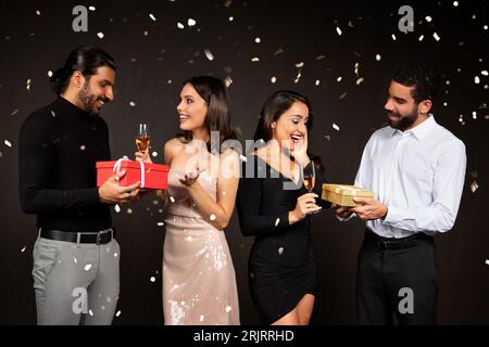 Zwei multirassische Paare feiern gemeinsam Weihnachten und tauschen Geschenke aus Stockfoto