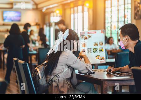 Rückblick auf junge asiatische Paare, die die Speisekarte lesen und gemeinsam essen. Ein junger Liebhaber las eine Karte im Restaurant, während er zu Mittag aß. Glückspaar Lo Stockfoto