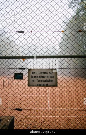 Vor dem Tennisplatz hängt ein Schild mit einem Kettengliederzaun. Der Tennisspieler schlägt den Ball über das Netz und macht Sport. Stockfoto