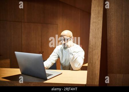 Porträt eines Reifen Mannes, der am Arbeitsplatz am Laptop mit Holzvertäfelung arbeitet Stockfoto