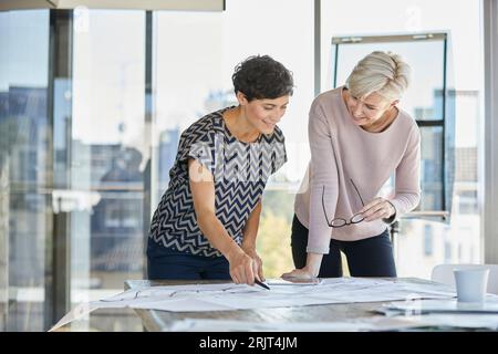 Zwei lächelnde Geschäftsfrauen, die über den Plan im Büro diskutieren Stockfoto