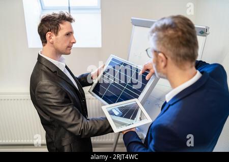 Zwei Geschäftsleute im Büro mit Solarzelle und Tablet diskutieren Stockfoto
