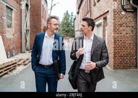 Zwei Geschäftsleute zu Fuß und im Gespräch mit einem alten Backsteingebäude Stockfoto