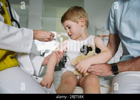 Kinderarzt injiziert Impfstoff in den Arm des unglücklichen Kleinkindes Stockfoto