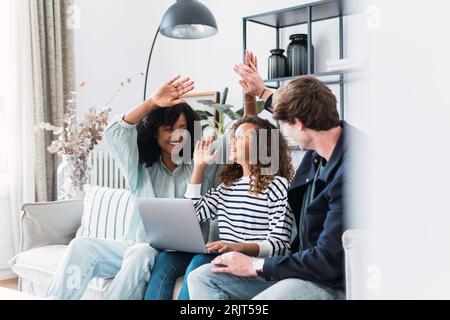 High Fiving glückliche Eltern sitzen auf dem Sofa mit Tochter mit Laptop Stockfoto