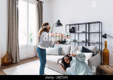 Glückliche Eltern spielen mit ihrer Tochter im Wohnzimmer den Buff eines blinden Mannes Stockfoto