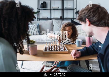 Eltern, die im Wohnzimmer sitzen und ihrer Tochter das Schachspielen beibringen Stockfoto