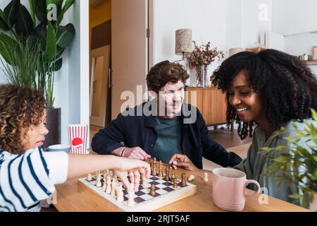 Eltern, die im Wohnzimmer sitzen und ihrer Tochter das Schachspielen beibringen Stockfoto