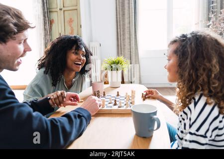 Eltern, die im Wohnzimmer sitzen und ihrer Tochter das Schachspielen beibringen Stockfoto
