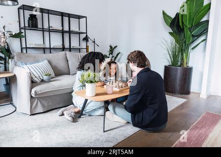 Eltern, die im Wohnzimmer sitzen und ihrer Tochter das Schachspielen beibringen Stockfoto