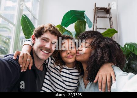 Eine fröhliche Familie fängt einen Moment zusammen in einem Wintergarten mit einem lustigen Selfie ein Stockfoto