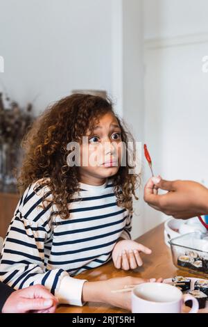 Überraschtes Mädchen, das sich anschaut, isst heißen Chilipfeffer, der von der Hand der Mutter gehalten wird Stockfoto