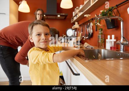 Lächelnder Junge, der zu Hause in der Küchenspüle die Hände wäscht Stockfoto