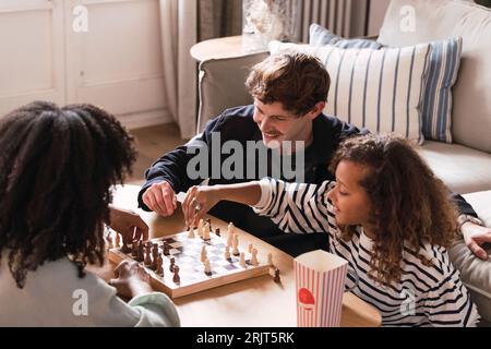 Eltern, die im Wohnzimmer sitzen und ihrer Tochter das Schachspielen beibringen Stockfoto