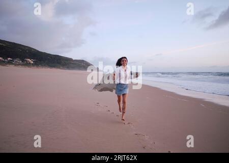Junge Frau, die am Strand auf Sand läuft Stockfoto