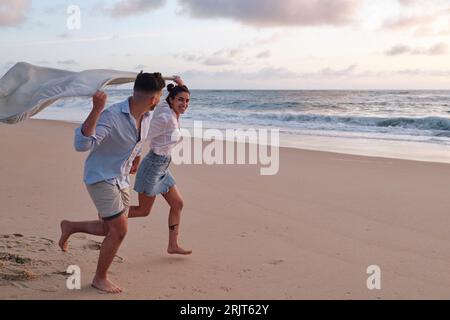 Mann und Frau laufen zusammen und halten am Strand eine Decke Stockfoto