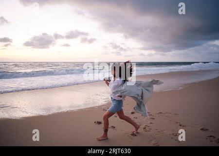 Eine sorgenfreie Frau, die am Strand auf Sand läuft Stockfoto