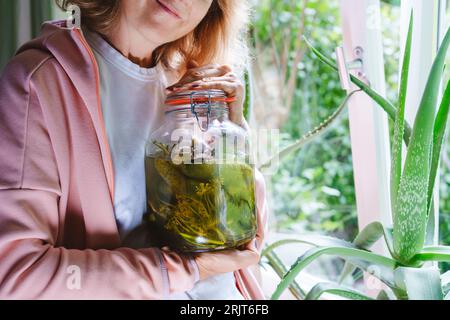 Reife Frau, die zu Hause ein Glas fermentierter Gurken hält Stockfoto