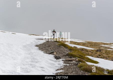 Verschneite Landschaft mit zwei Wanderern, die im Hintergrund in Sierra Nevada spazieren Stockfoto