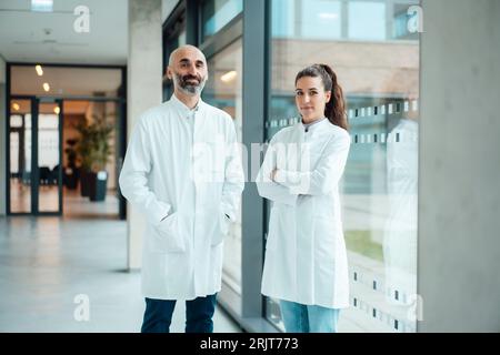 Lächelnde Ärzte, die am Glasfenster im Flur stehen Stockfoto