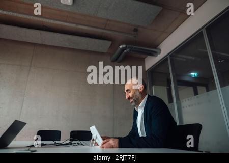 Lächelnder, reifer Geschäftsmann, der Tablet-PC am Schreibtisch nutzt Stockfoto