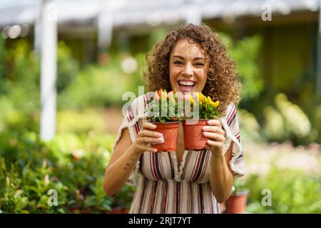 Glückliche Frau, die rote und gelbe Pfefferpflanzen in der Baumschule hält Stockfoto